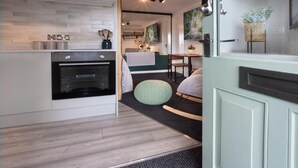 A modern kitchen with a built-in oven, a dining area with a table and chairs, and a cozy seating area with a rocking chair. - Eden Escape - Comfy Apartment Quiet Neighbourhood (Kendal)