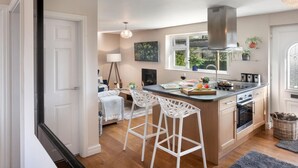 A modern kitchen with a central island, bar stools, a stove, and a large window. - Scar View - Getaway for Two (Kendal)