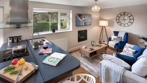 A modern kitchen with a central island, a dining area with a blue sofa, and a living room with a blue armchair. - Scar View - Getaway for Two (Kendal)