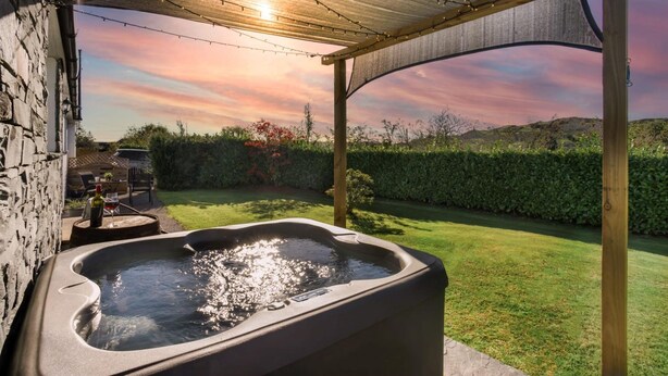 A hot tub under a pergola with a sunset view, surrounded by a well-maintained lawn and stone walls. - Scar View - Getaway for Two (Kendal)