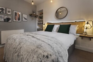 A bedroom with a large bed, a round mirror, and wall-mounted shelves with plants. - Windermere Central Hotel - Room 6 (Windermere)