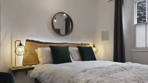 A bedroom with a wooden headboard, a round mirror, a fluffy white throw blanket, and two bedside lamps. - Windermere Central Hotel - Room 6 (Windermere)