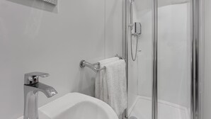 A modern bathroom with a glass-enclosed shower, a white sink, and a towel rack. - Windermere Central Hotel - Room 6 (Windermere)