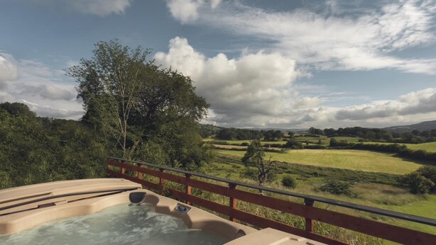 A hot tub with a wooden deck and a scenic view of rolling hills and trees. - Lyth Valley Country House - 9 Rooms (Kendal)