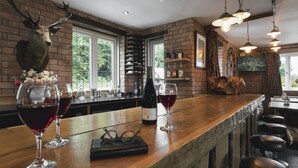 A rustic bar area with a wooden countertop, wine glasses, a bottle of wine, and a deer head mounted on the wall. - Lyth Valley Country House - 9 Rooms (Kendal)