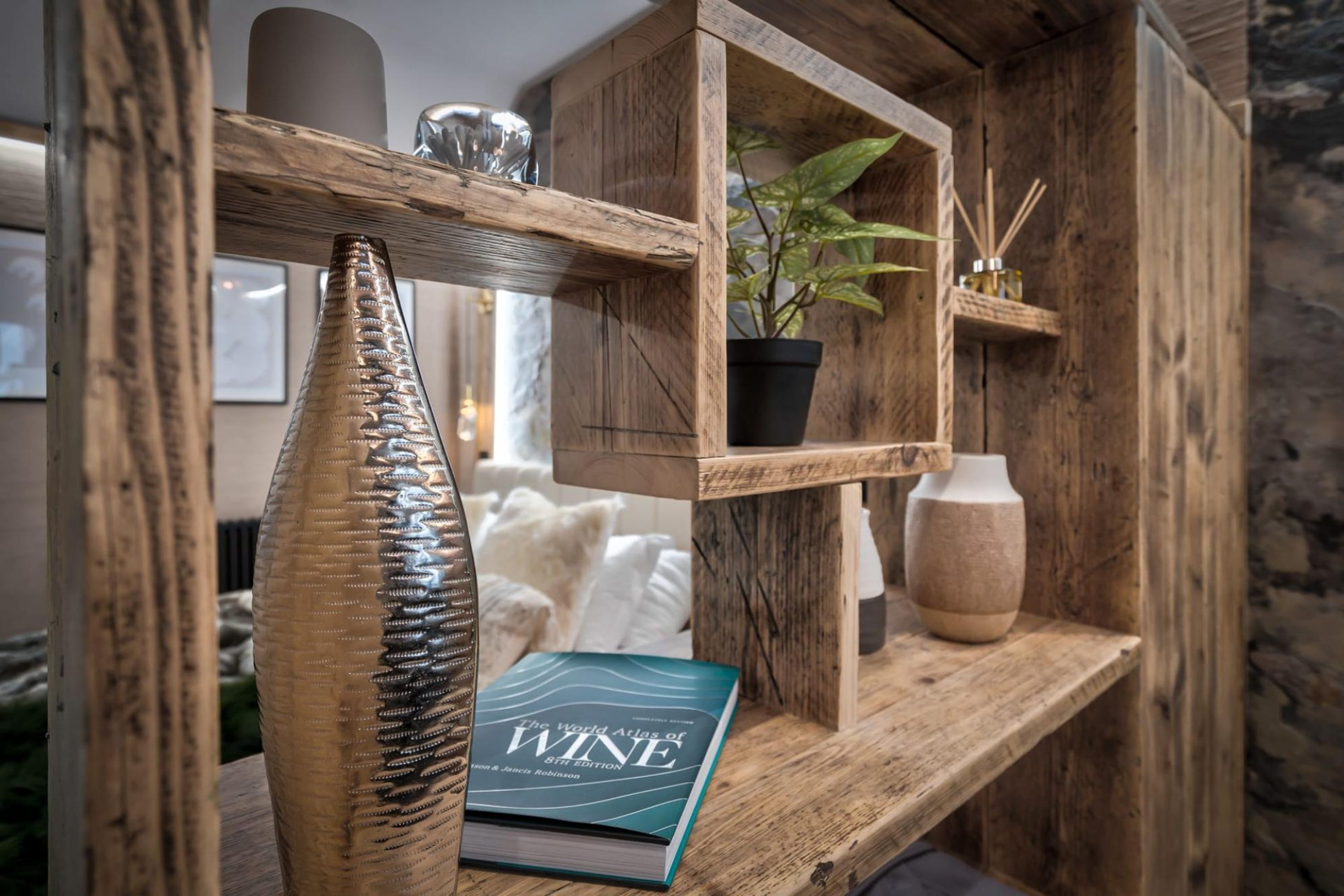 A wooden shelf with a book titled 'The World Atlas of Wine', a potted plant, and a vase.