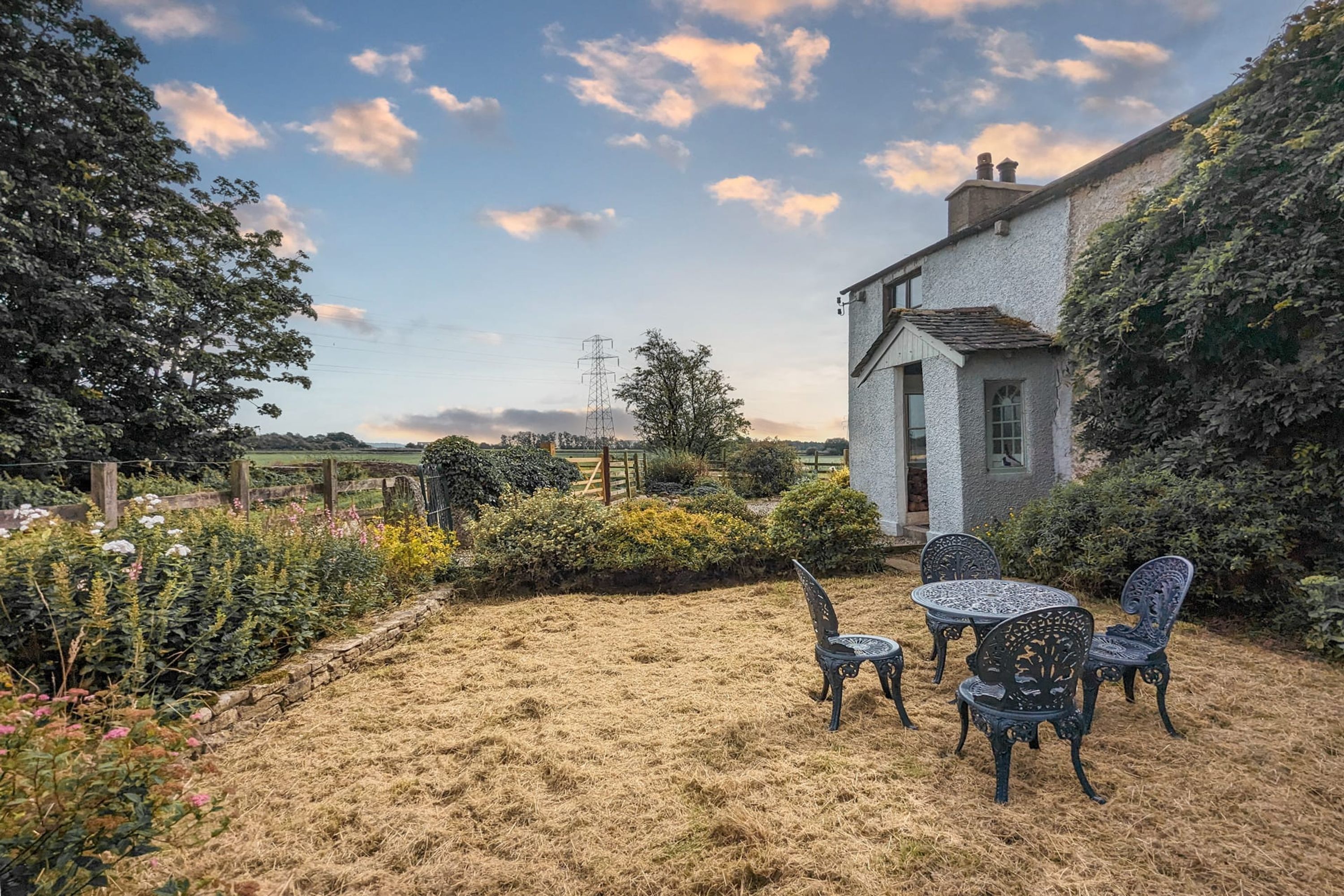 Un jardin avec une table et des chaises, un bâtiment blanc et une ligne électrique en arrière-plan.