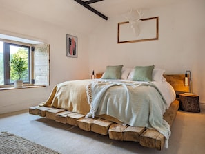A bedroom with a wooden platform bed, a window with a view of greenery, a framed deer head on the wall, and a bedside lamp.