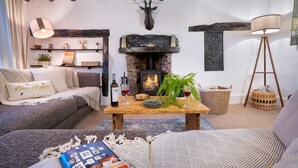 Uma sala de estar acolhedora com lareira, um sofá, uma mesa de centro com livros e uma luminária, além de objetos decorativos.
