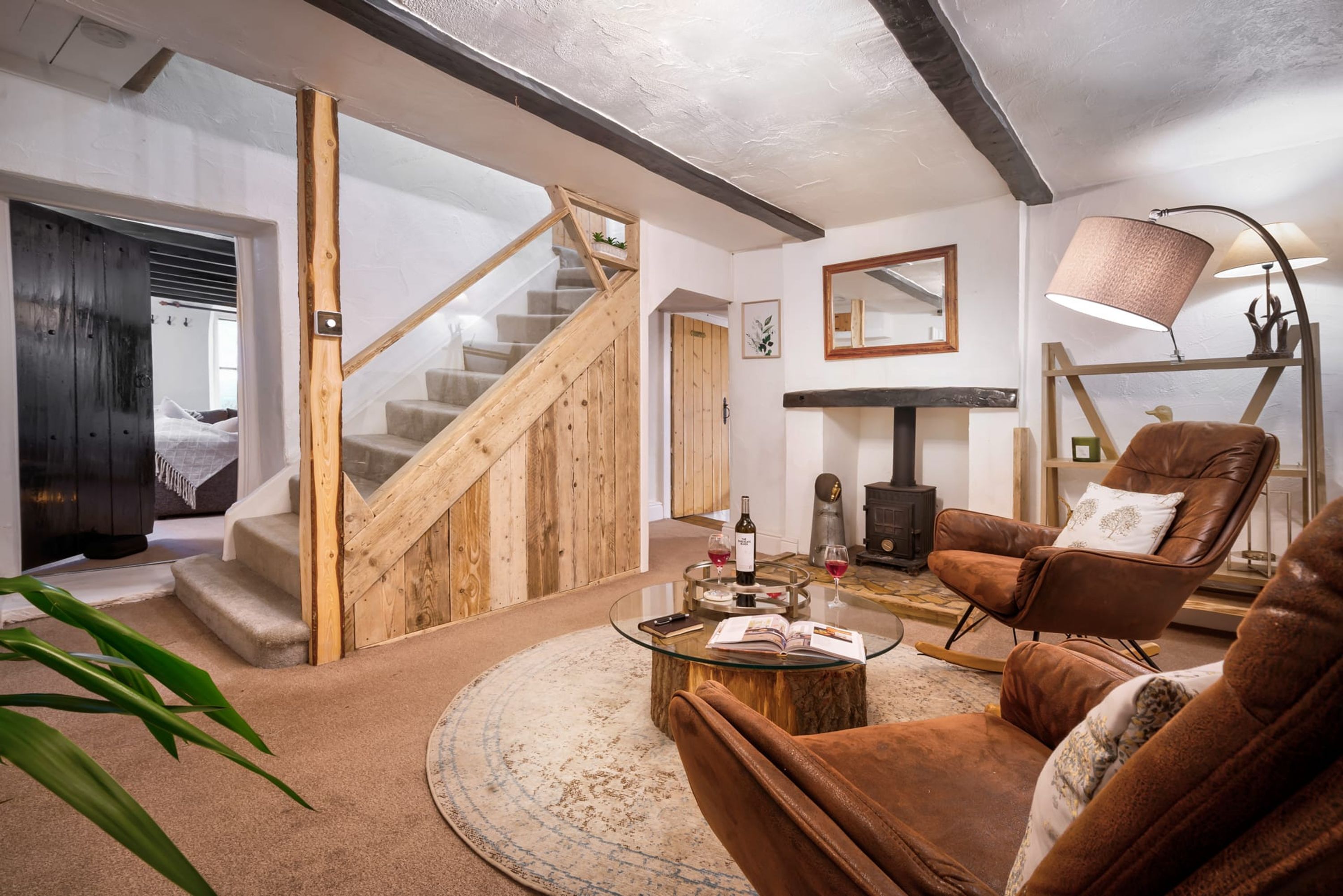 A cozy living room with a wooden staircase, a leather armchair, a glass coffee table, and a fireplace.