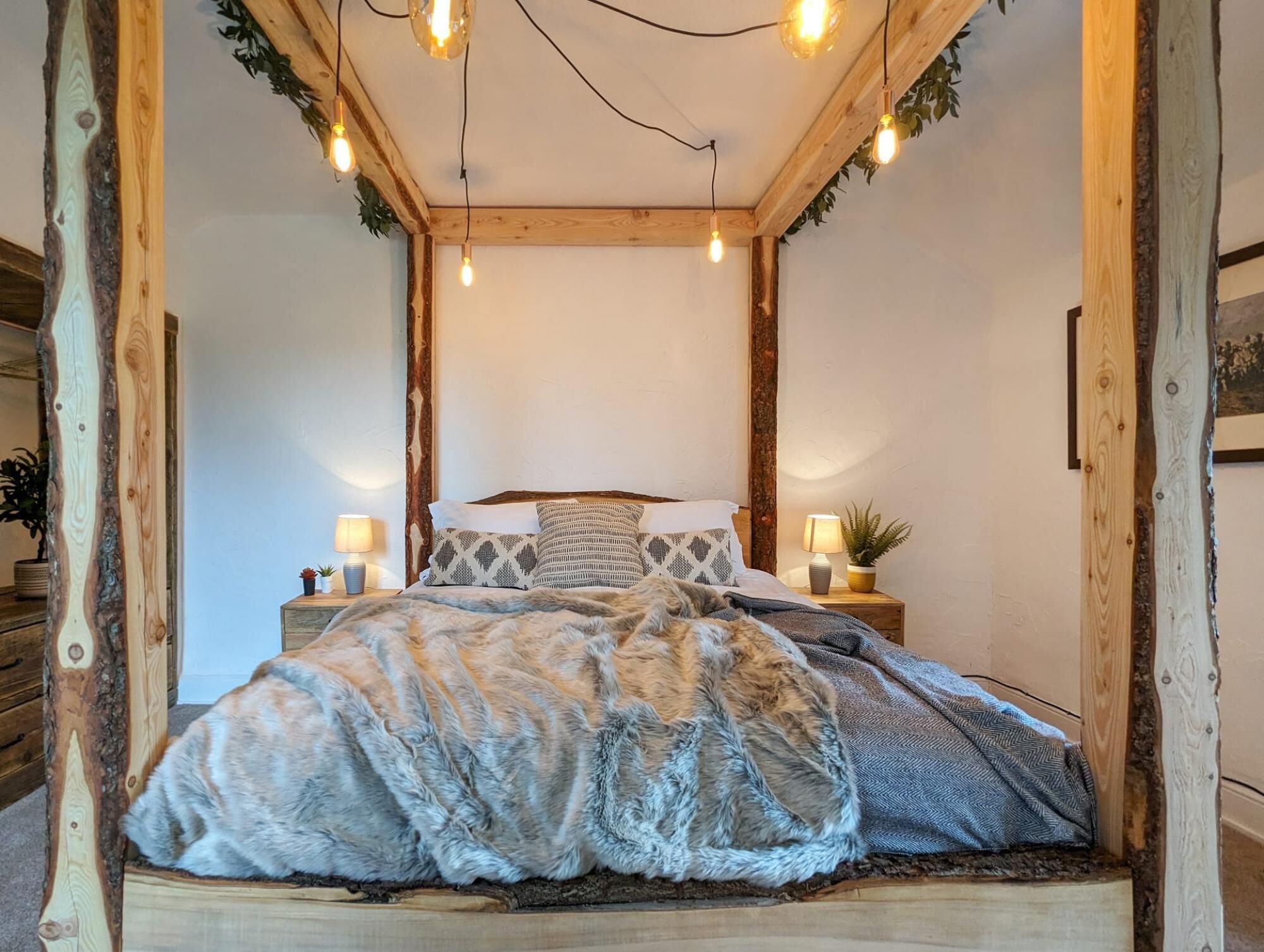 A cozy bedroom with a wooden bed frame, a fluffy blanket, and a nightstand with a lamp.
