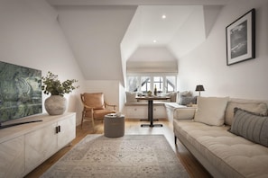Un loft espacioso con techo alto, un ventanal grande, una zona de estar acogedora con sofá y sillones, una mesa de comedor y un televisor sobre un mueble.