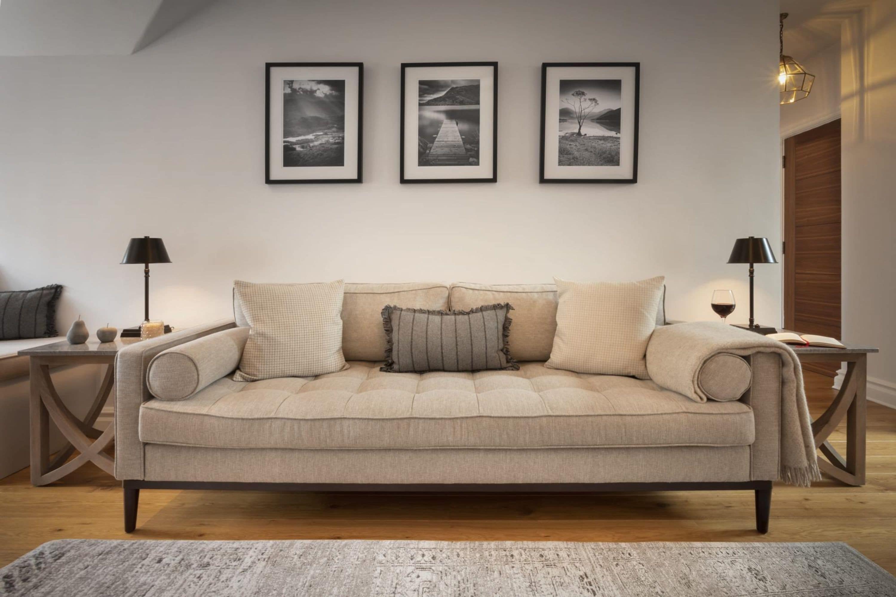 A neutral-toned living room with a beige sofa, a patterned rug, and three framed photographs on the wall.