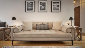 A neutral-toned living room with a beige sofa, a patterned rug, and three framed photographs on the wall.