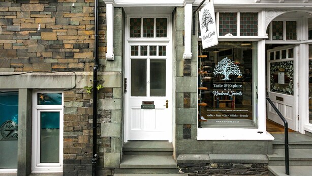 A building with a stone facade, a white door, and a sign advertising a distillery.