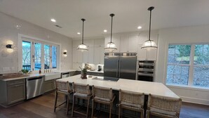 Une cuisine moderne dotée d’un grand îlot central, d’appareils électroménagers en acier inoxydable et de luminaires suspendus.