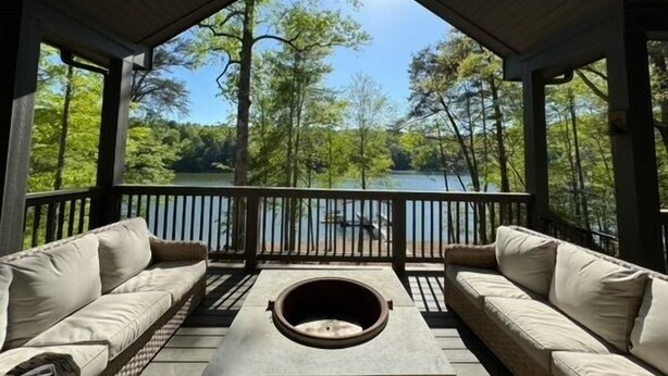 Un espace extérieur aménagé, abrité et doté d’un foyer, offrant une vue sur un lac entouré d’arbres.