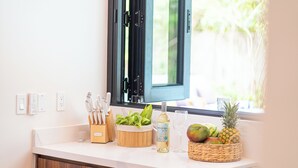 Un plan de travail de cuisine avec un range-couteaux, un saladier rempli de légumes verts, une bouteille de vin, un verre et un panier de fruits.