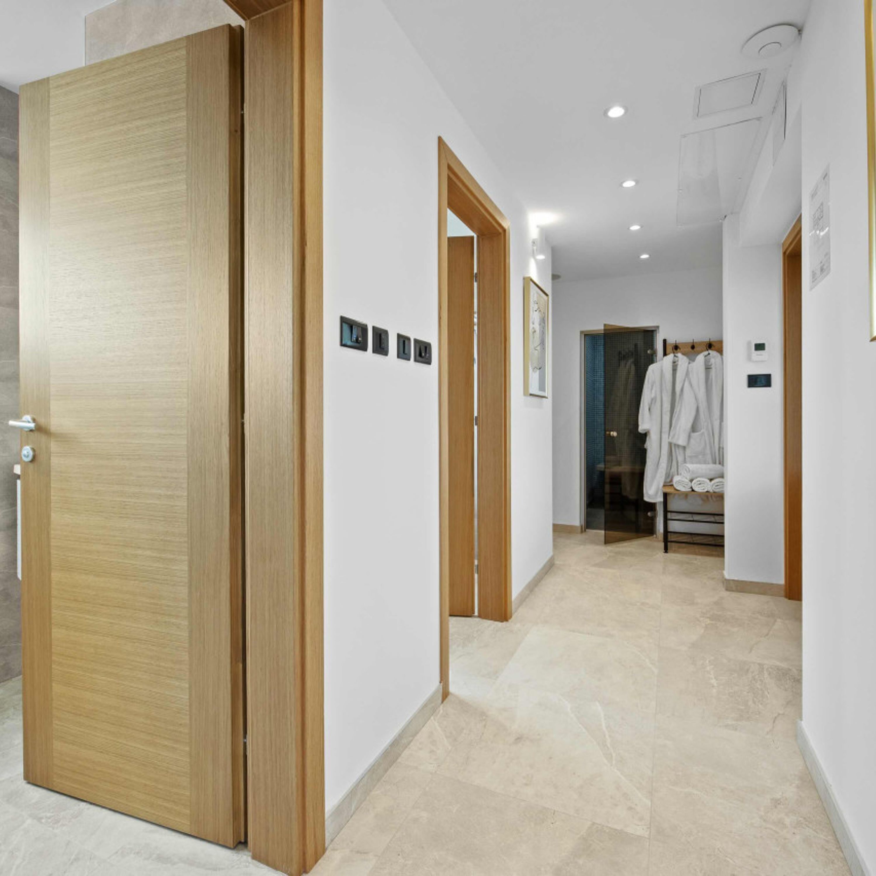 A modern hotel corridor with wooden doors, a tiled floor, and a visible bathroom with towels.