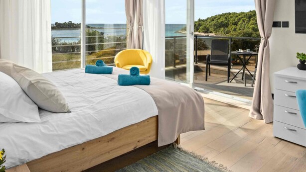 A modern bedroom with a large bed, a yellow chair, and a balcony with a view of the sea. - Villa Palma - Seaside Luxury Villa for 6 Person (Pula)