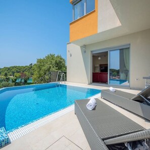 A modern outdoor swimming pool with lounge chairs and a view of a lush landscape. - Villa Magnolija in Pula (Pula)