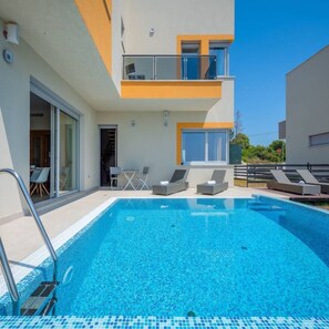 A modern building with a swimming pool, outdoor seating, and a balcony. - Villa Magnolija in Pula (Pula)