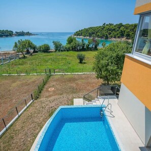 A modern building with a swimming pool, a view of the sea, and a grassy area with trees. - Villa Magnolija in Pula (Pula)