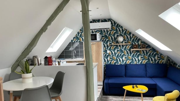 A compact living space with a dining area, a blue sofa, and a small yellow table. - L'Auberge de papa (Auzouville-sur-Ry)