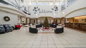 Eine geräumige Lobby mit einem zentral platzierten Weihnachtsbaum, einem 'Welcome'-Schild und Wandmalereien mit Mickey Mouse.