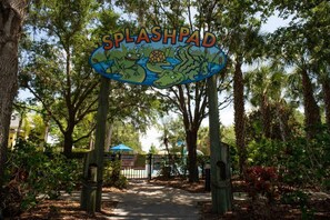 Un panneau indiquant l’emplacement d’un parc aquatique, avec un thème tropical, entouré d’arbres et bordé d’un sentier.