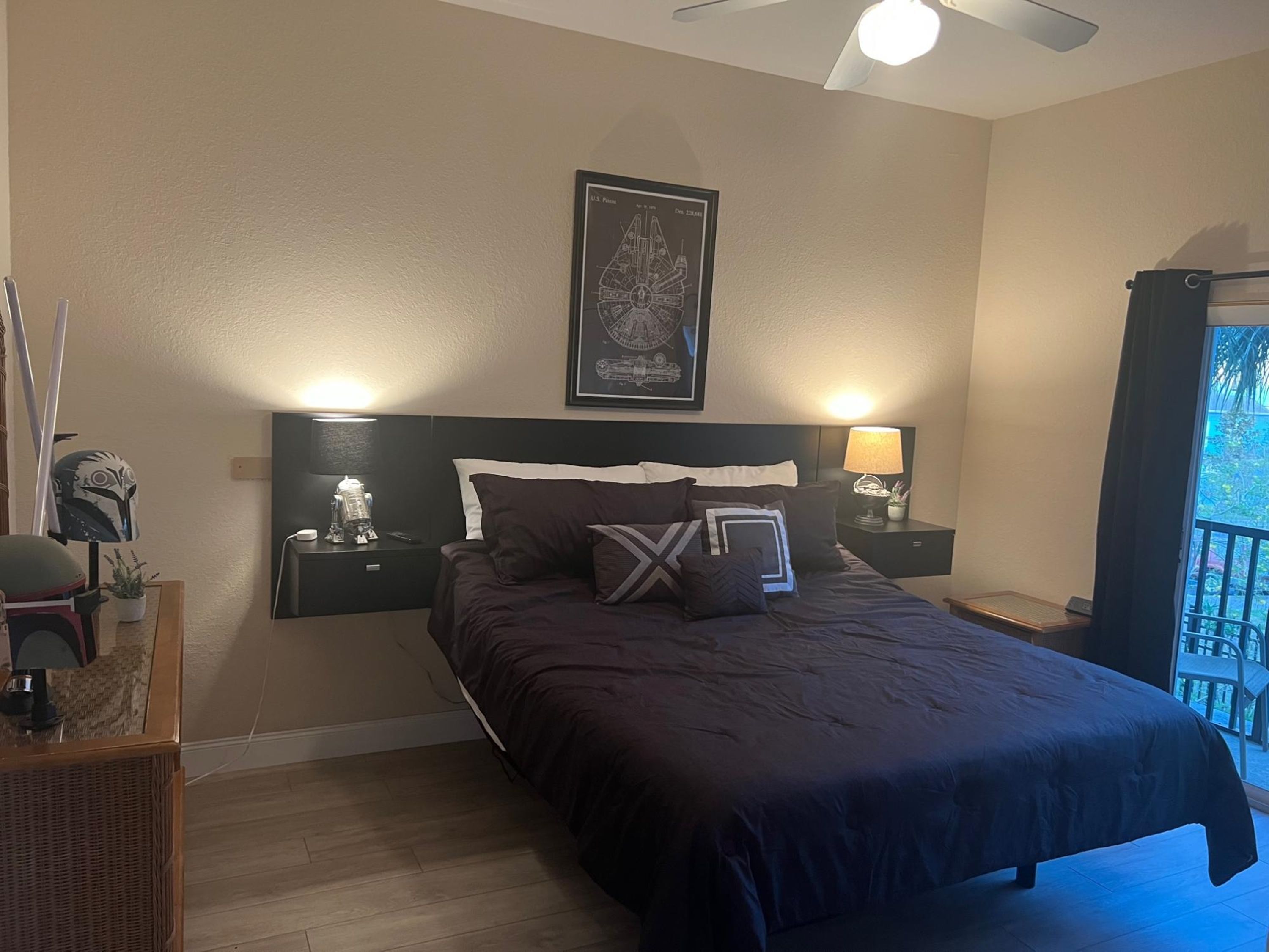 Una camera da letto con un letto grande, due comodini con lampade, una ventola a soffitto, una mappa incorniciata al muro e un balcone con vista.