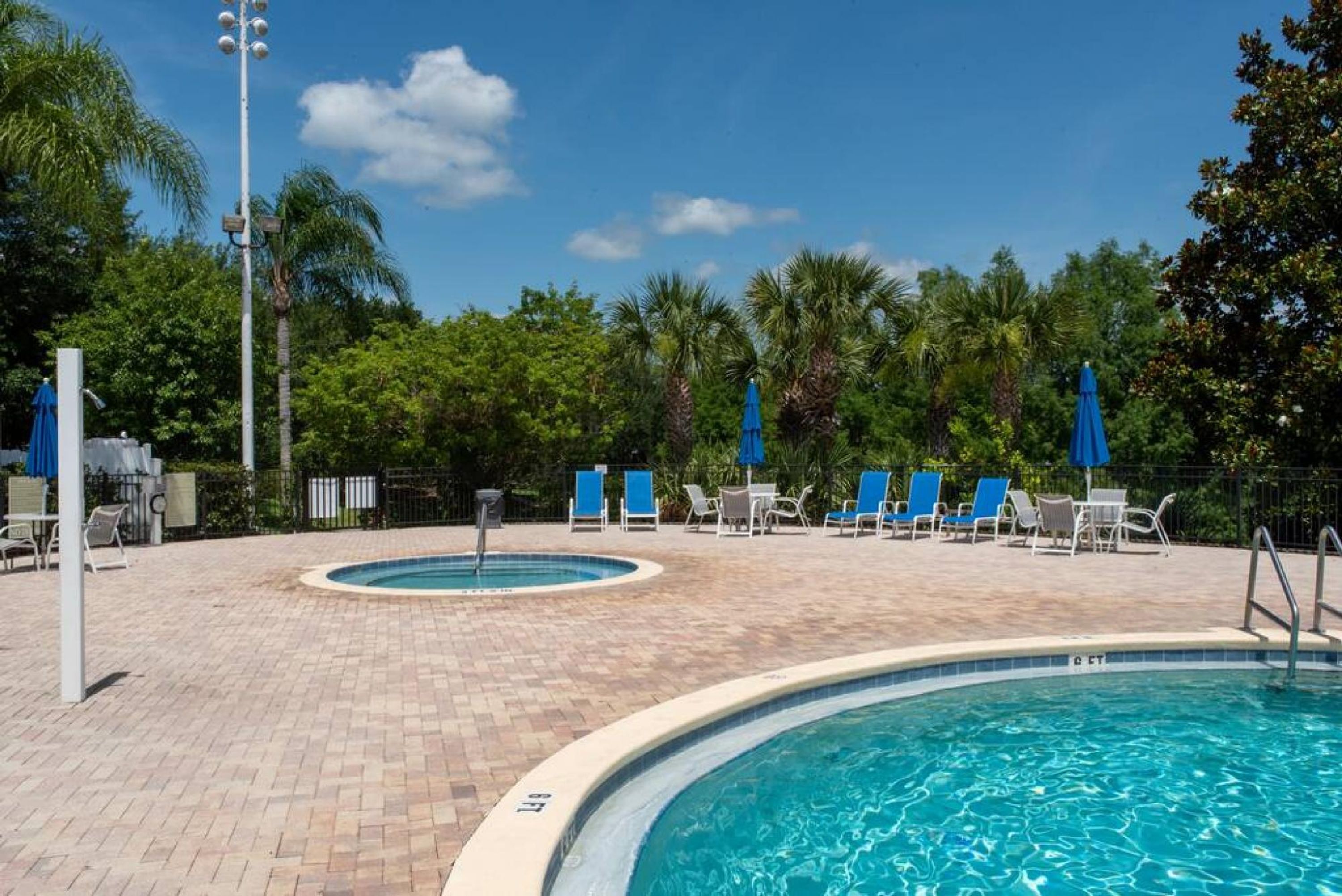 A pool area with blue chairs and umbrellas, surrounded by palm trees and a clear sky.