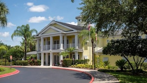 A yellow building with a balcony, surrounded by greenery and a curved driveway.