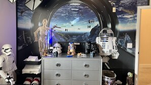 A Star Wars-themed room with a large mural of space and spacecraft, a dresser with drawers, and various Star Wars figurines.