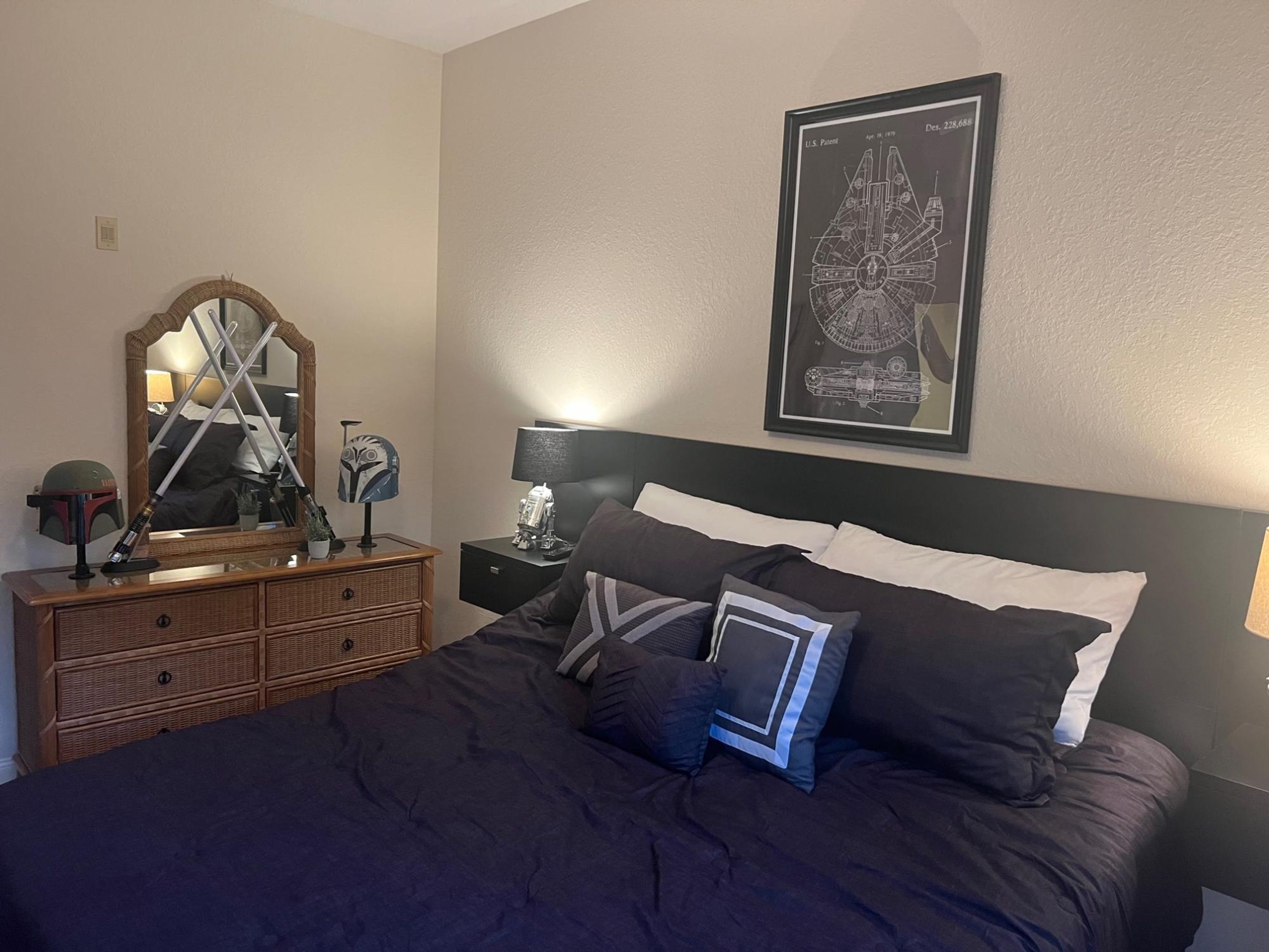 A bedroom with a large bed, a dresser, a mirror, a Star Wars poster, and a lamp.