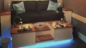 A compact living space with a black sofa, two side-by-side sinks, and a small wooden countertop.