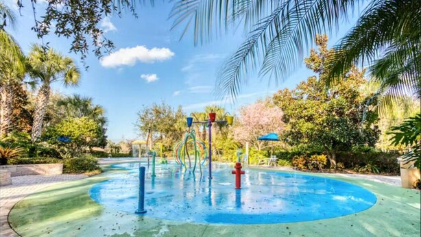 A water play area with a circular pool, surrounded by palm trees and greenery.