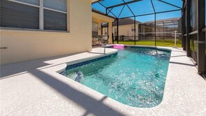 En swimmingpool med glasafskærmning, en overdækket terrasse og udsigt til omkringliggende huse.