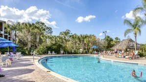 A swimming pool with lounge chairs and umbrellas, surrounded by palm trees and a thatched-roof structure. - Disney Area Grnd Floor Park Free (Davenport)