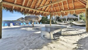 A beachside area with a ping pong table, lounge chairs, and a hammock under a thatched roof. - Disney Area Grnd Floor Park Free (Davenport)