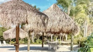 Une zone de plage avec des parasols en chaume et un banc en bois.
