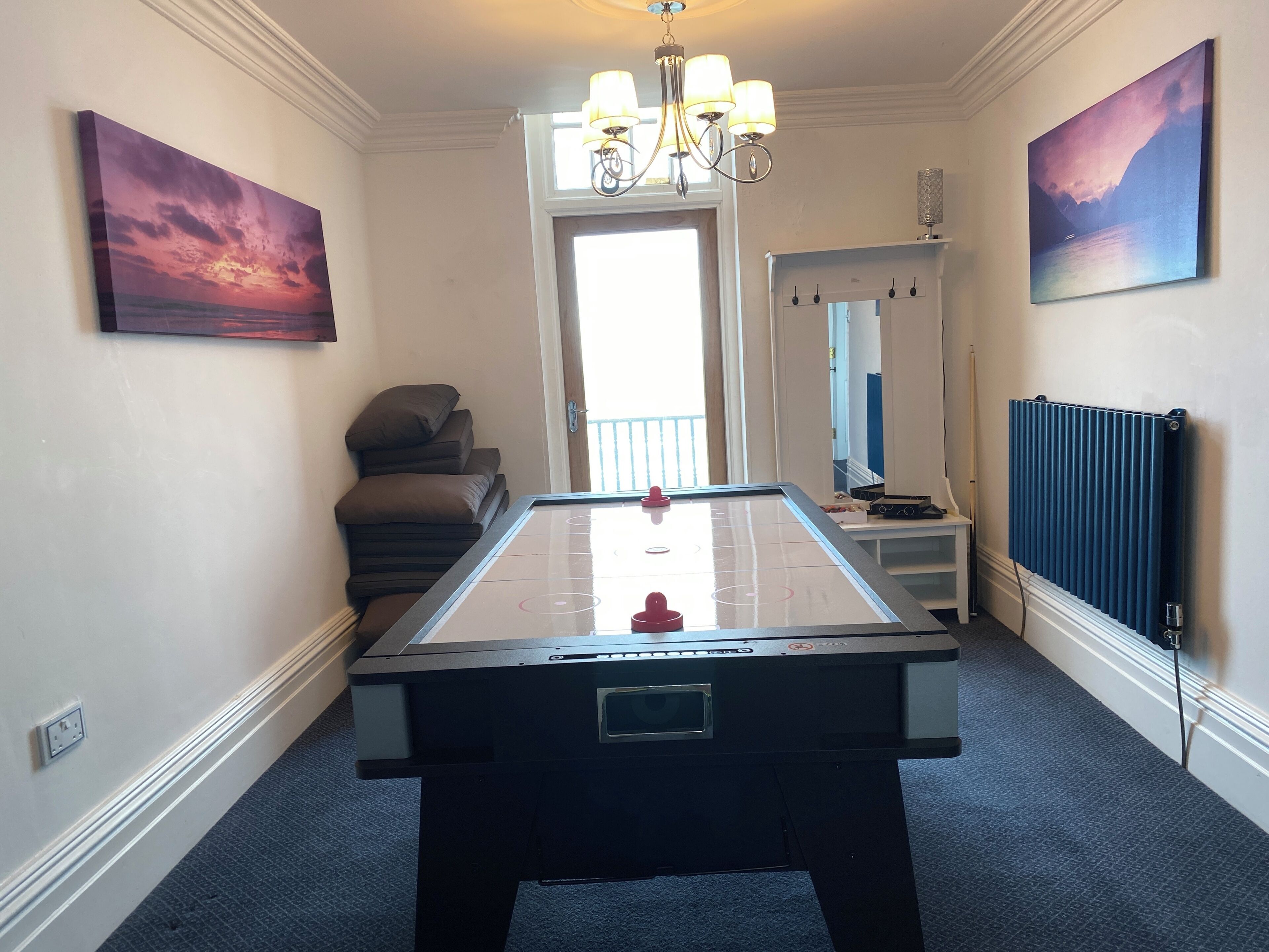 A room with a foosball table, a chandelier, and two paintings on the walls.