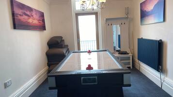 A room with a foosball table, a chandelier, and two paintings on the walls.
