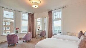 A hotel room with a large bed, two chairs, a small table, and a view of the sea.