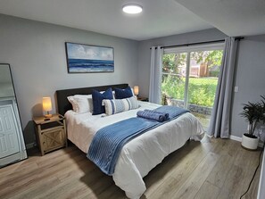 A bedroom with a bed, nightstands, a painting, a window with curtains, and a potted plant. - Holland Hydrotherapy Spa & Fire Pit Retreat (Holland)