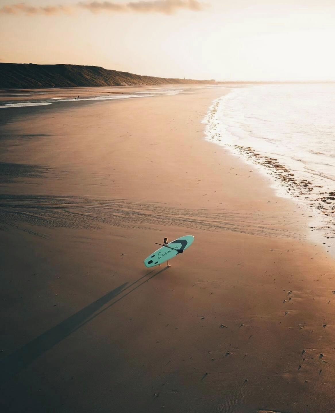 En strand med et surfbræt og en person, der går i sandet.