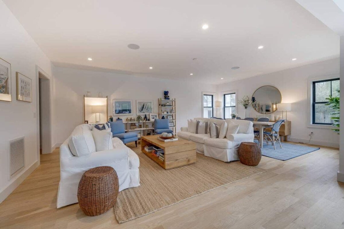 A spacious living room with two white sofas, a coffee table, and a dining area with a round table and chairs.