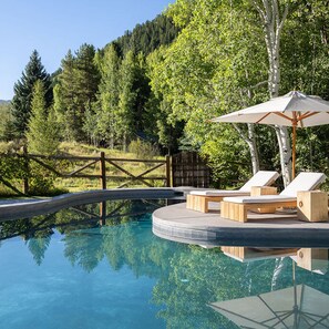 Relax by the serene pool surrounded by lush greenery and a wooden fence, with lounge chairs and a shaded area.