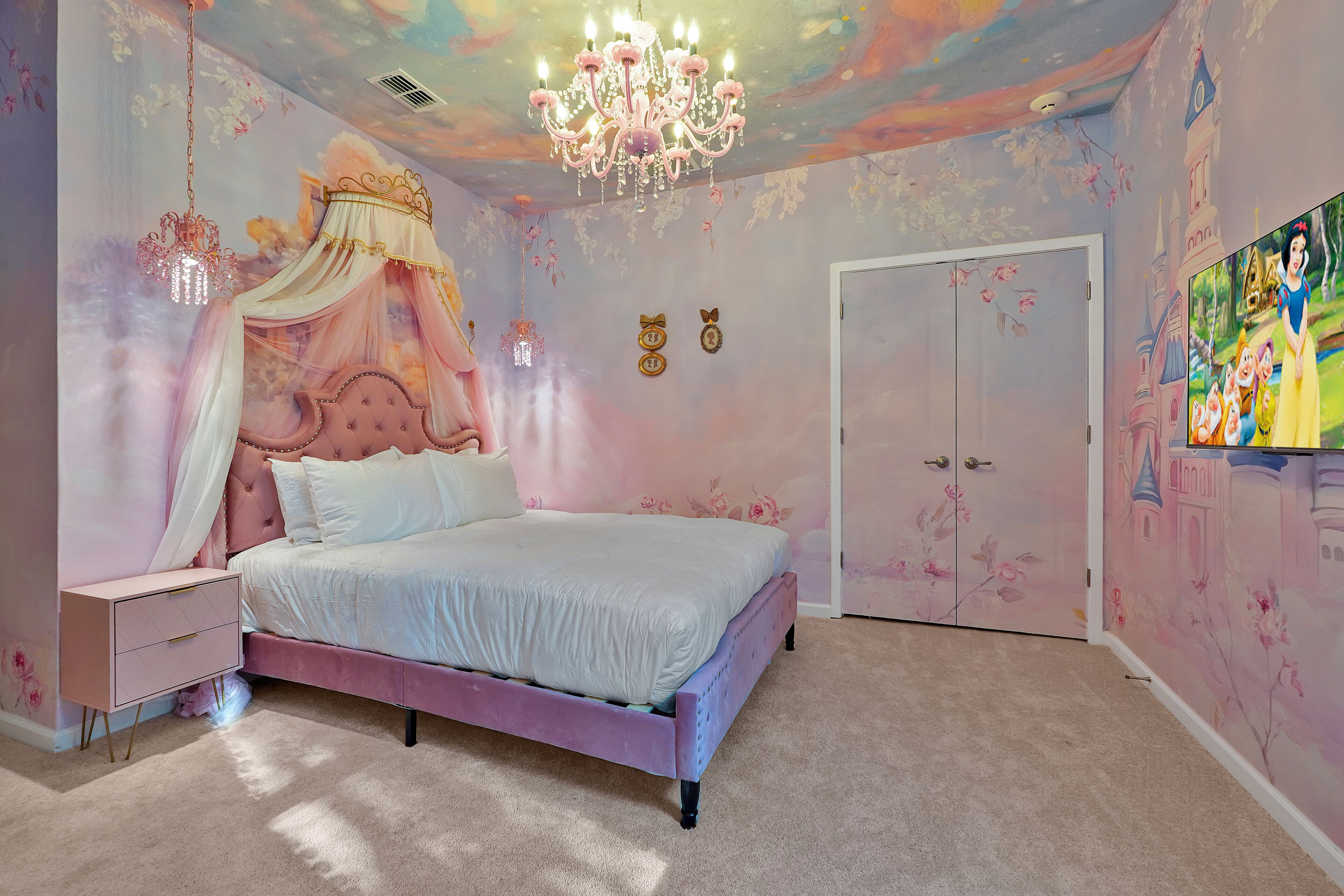 A bedroom with a pink canopy bed, a chandelier, and floral wall art.