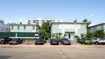 Fila de edificios modernos de dos pisos con números en las puertas, coches aparcados y un seto verde.